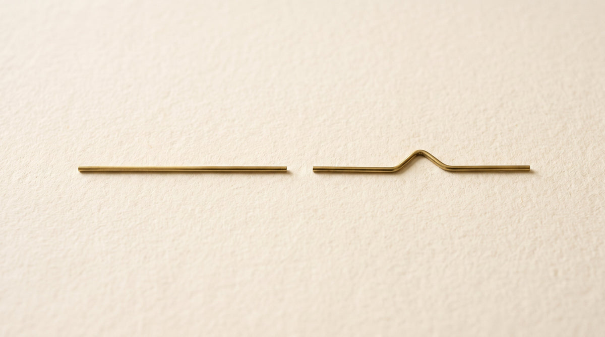 Zwei dünne goldene Drahtstücke im Vergleich: eine gerade Linie und eine geknickte Form symbolisieren die all-trans- und cis-Struktur von Vitamin K2 MK-7