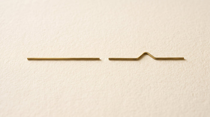 Zwei dünne goldene Drahtstücke im Vergleich: eine gerade Linie und eine geknickte Form symbolisieren die all-trans- und cis-Struktur von Vitamin K2 MK-7